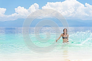 Young european woman in bikini with good mood splashing and dancing in beautiful tropical calm sea under cloudy soft sky