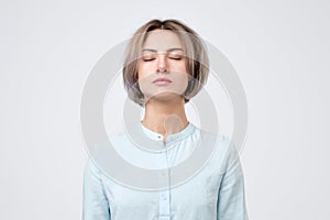 Young european woman in blue shirt closing eyes. No emotion on her face.