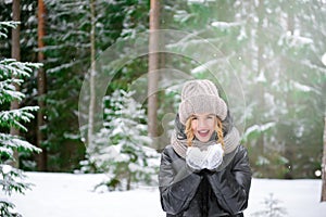 Young European woman in a jacket and hat in the forest in winter , fir under the snow