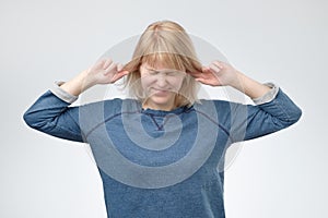 Young european woman plugging ears, looking up, pretending not to hear what she is told