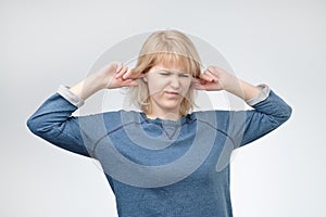 Young european woman plugging ears, looking up, pretending not to hear what she is told