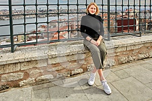 Young European woman poses against backdrop of cityscape while walking around Istanbul.