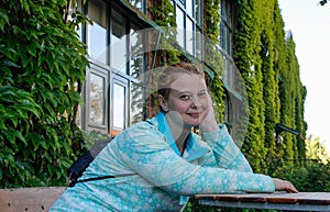 A young European woman with red hair and traces of acne on her face sits at a table in the garden. Very beautiful and fabulously c