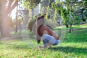 Young European woman is sitting on a grass and doing yoga exercise. Healthy lifestyle outdoors
