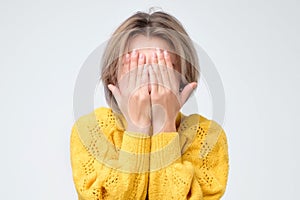 Young european woman in yellow sweater hides her face