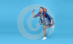 Young excited Asian man traveler running with backpack passport and boarding pass ready to fly on isolated blue background