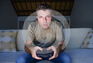 Young excited and concentrated man at home playing videogames holding controller looking stressed and focused in video gaming