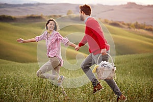 A young excited couple running on a meadow holding by hands while going to picnic. Relationship, love, together, picnic, nature