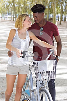 Young excited couple walking with bike through park