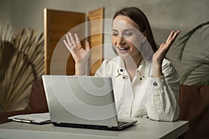 Young, excited, happy brunette woman in a white shirt who has achieved success using a laptop, winning online at home