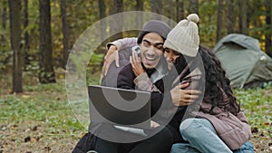 Young excited happy family couple in love sitting in nature reading good news on laptop surprised rejoicing at victory