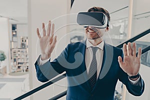 Young excited man office worker using virtual reality simulator at work, moving hands in air