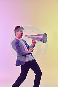Young excited man shouting in megaphone, having fun isolated over light background in neon light. Concept of emotions