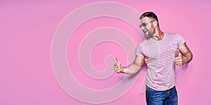 Young excited man on vacation over pink background pointing finger to the side with successful idea.