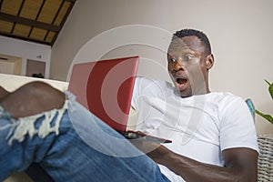 Young excited and surprised young black afro American man in disbelief and shock face expression networking with laptop computer