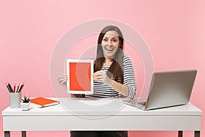 Young excited woman hold tablet computer with blank empty screen sit work at white desk with contemporary pc laptop