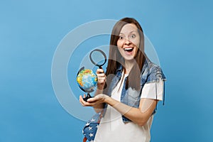 Young excited woman student in denim clothes with backpack looking on world globe with magnifying glass learn about