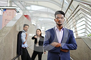 Young executive standing with arms crossed is suspiciously, background are employee talking about him as bullying