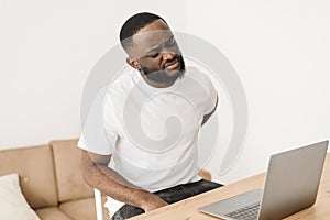 Young exhausted african american worker is experiencing back discomfort due to long work at the desk in the home office