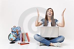 Young exhausted angry woman student holding laptop pc computer and spreading hands sitting near globe, backpack, school