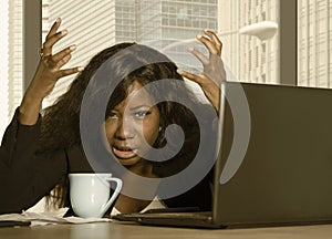 Young exhausted and depressed black African American businesswoman working upset and sad at office computer desk by the window in