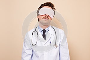 Young exhausted doctor man in sleeping mask after hard worlking day