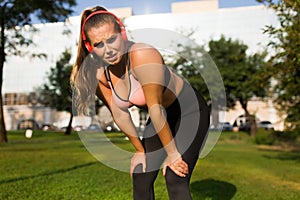 Young exhausted plus size woman in sporty top and leggings with red headphones tiredly looking in camera while leaning