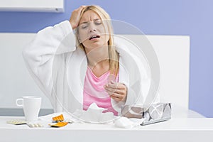 Young exhausted woman suffering from headache and cold in kitchen