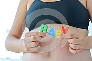 Young expectant mother with letter blocks spelling baby on her pregnant belly