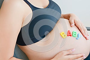 Young expectant mother with letter blocks spelling baby on pregnant belly