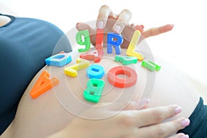 Young expectant mother with letter blocks spelling girl on her pregnant belly