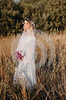 A young expectant mother in the third trimester of pregnancy with a bouquet of flowers in her hands, in a white dress