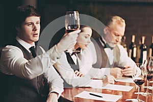 Young experienced sommelier looks at sediment of wine in glass. Wine tasting.