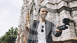 Young but experienced traveller is making selfie near the church in the city. The guy smiles and looks happy