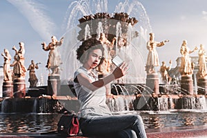 Black girl is photographing herself in front of a fountain