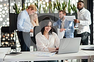 Young exuberant female office worker looking at camera with lovely smile at her workplace in meeting room