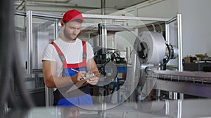 Young factory man in uniform making notes on clipboard at water production factory