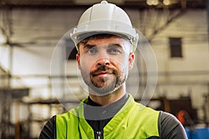 Young factory worker in hard hat standing at industry site