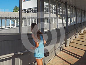 A young fair haired girl stands in a long corridor and looks out the window