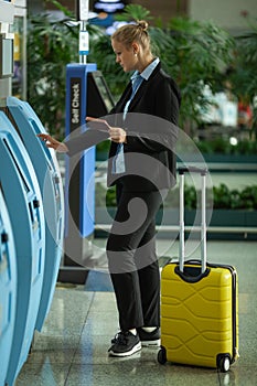 A young fair haired woman in an airport near the self check terminal