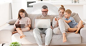Young family addicted with gadgets relaxing on sofa at home