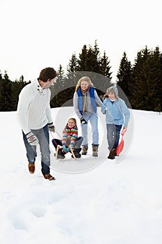 Young Family In Alpine Snow Scene With Sled