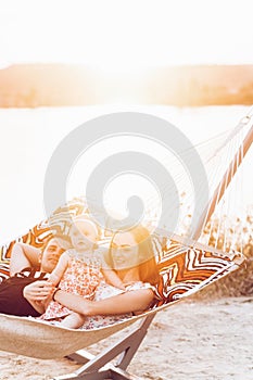 Young family with baby on the beach, smiling father and mother holding cute little girl while lying in a hammock, hipster family