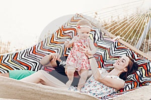 Young family with baby on the beach, smiling father and mother holding cute little girl while lying in a hammock, hipster family