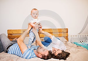 Young family with a baby boy at home, lying on bed.