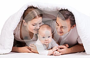 Young family with baby boy under blanket on bed