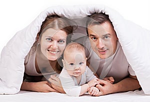 Young family with baby boy under blanket on bed