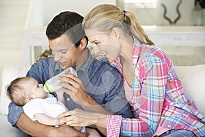 Young Family With Baby Feeding On Sofa At Home