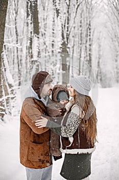 Young family with baby son on hands standing in winter forest