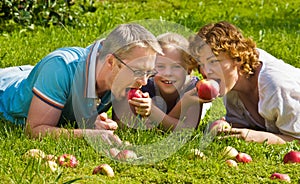 Young family bites apple, lie on a grass